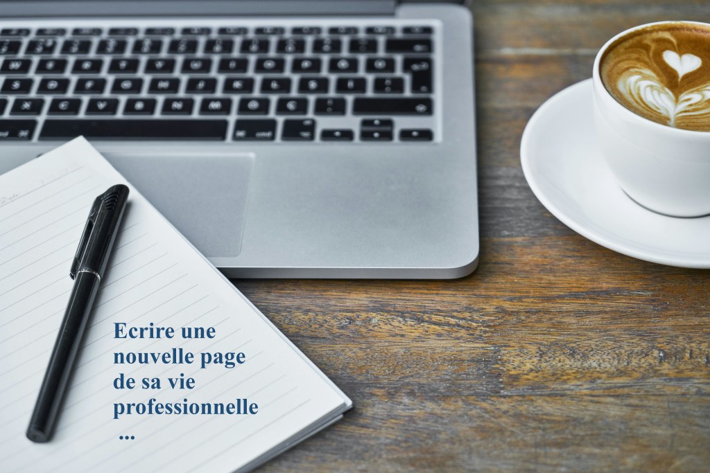 Photo d'un bureau avec un ordinateur, un café latté et un cahier sur lequel il est écrit "Ecrire une nouvelle page de sa vie professionnelle ..."