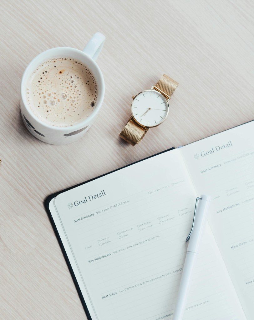 Photo en prise de dessus d'un bureau avec agenda et tasse de café. Cette photo symbolise sobrement le travail et la productivité.